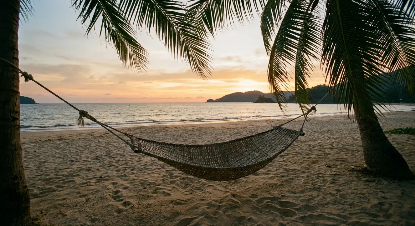 Sonnenuntergang über einer Hängematte am Strand, leichte Brise bewegt die Palme im Vordergrund, warme Farbtöne