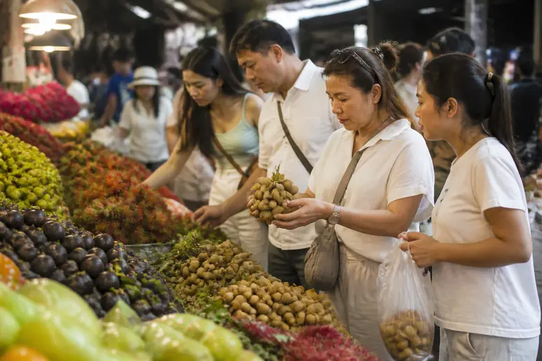 Thai-Touristen wählen auf einem Markt in Chiang Mai sorgfältig frisches Obst aus, umgeben von bunten Produkten und einheimischen Einkäufern.