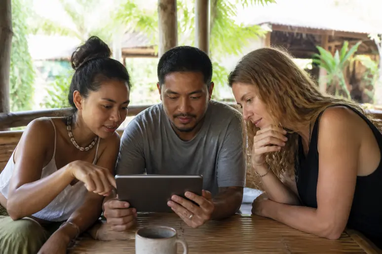 Thailänder vergleichen Mietpreise für Ferienwohnungen auf Koh Phangan auf einem Tablet in einem Café.