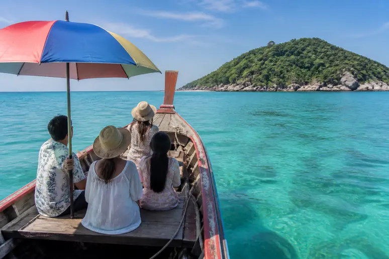 Einheimische Thais reisen mit einem Longtail-Boot durch das kristallklare Wasser auf dem Weg zu einer malerischen Insel im Marine Park.