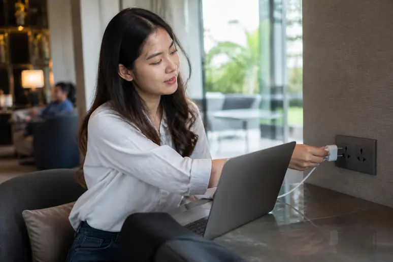Eine junge Thailänderin steckt in einem modernen Hotel in Bangkok ihren Laptop in eine Universalsteckdose, europäischer Stecker passt.