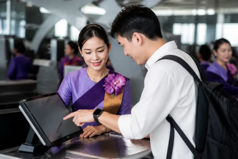 Eine Flugbegleiterin von Thai Airways hilft einem Reisenden bei der Sitzplatzreservierung am Schalter.