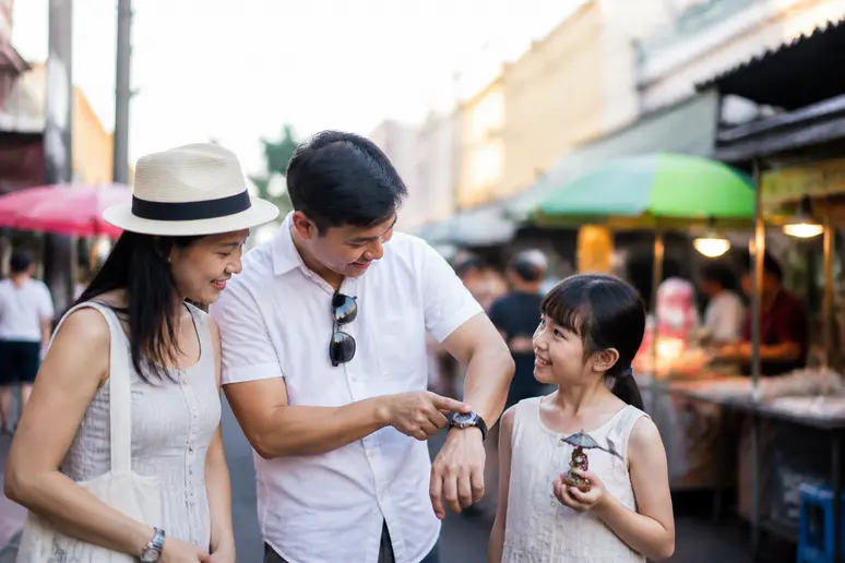Thailändische Familie in Bangkok nutztuhren, um den Zeitunterschied zu Deutschland zu erklären, während sie einen Markt besuchen.