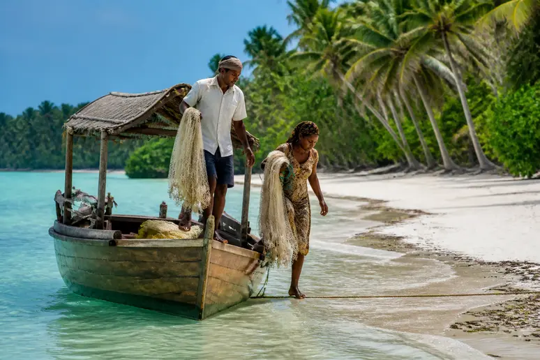 Beste Reisezeit Malaysia für Ostküste: Fischer laden Boote an sonniger Küste mit türkisblauem Wasser.