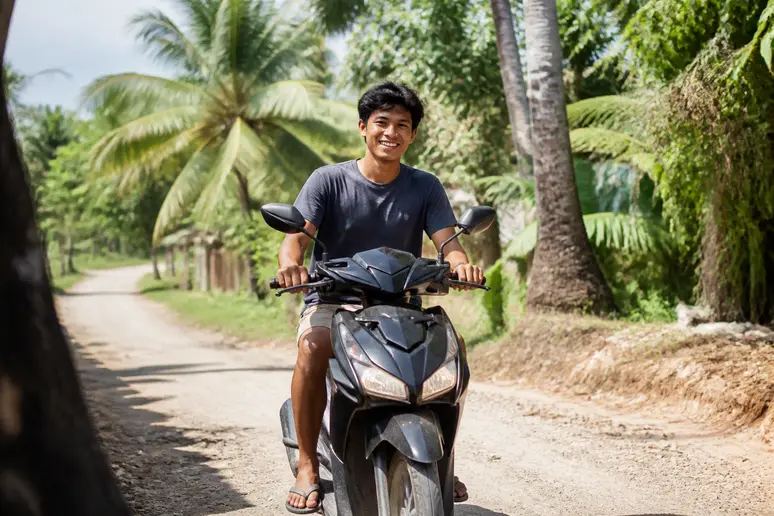Ein lokaler Mann fährt auf Nusa Lembongan mit einem Roller auf einer schmalen Straße, praktischer Tipp für die Inselerkundung.