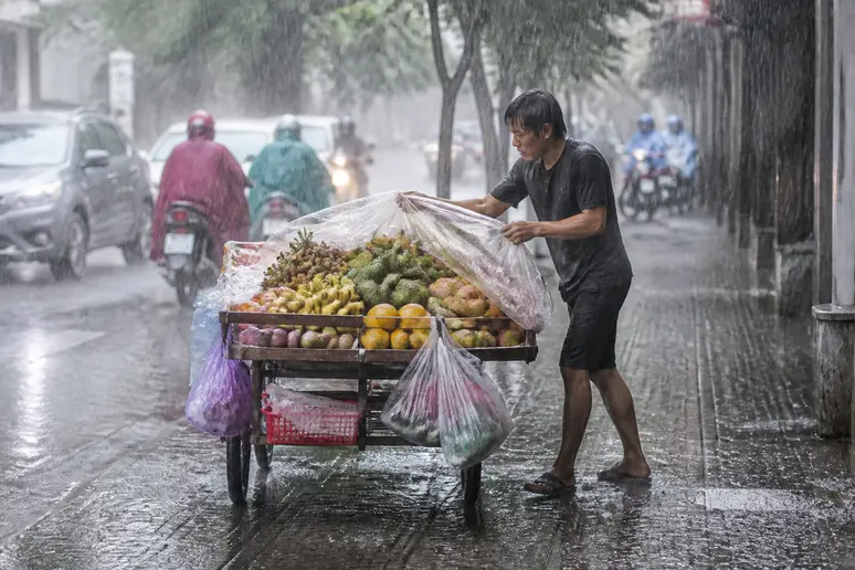 Straßenverkäufer packt Obst in Saigon während eines kurzen Schauers der regenzeit vietnam.