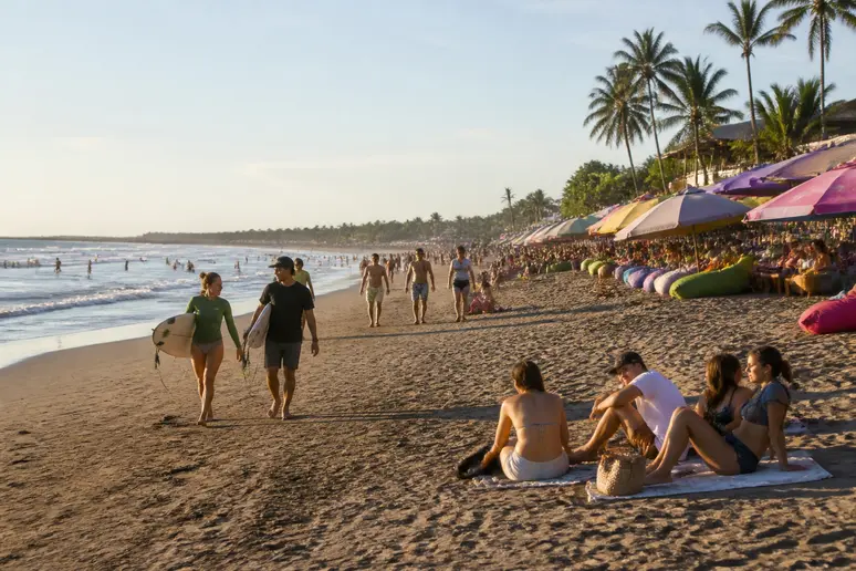 Surfer lernen in Seminyak das Wellenreiten am breiten Sandstrand bei entspannter Atmosphäre.