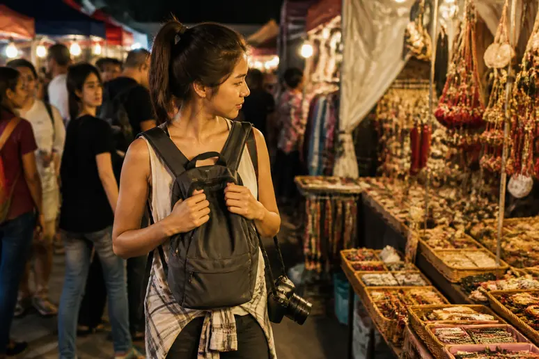 Frau achtet auf Sicherheit in einem belebten Nachtmarkt während des Backpacking Thailand, typisches Sightseeing.