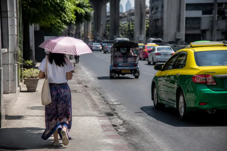 Fußgänger mit Sonnenschirm auf einem heißen Gehweg in Bangkok während der Hitzeperiode im April