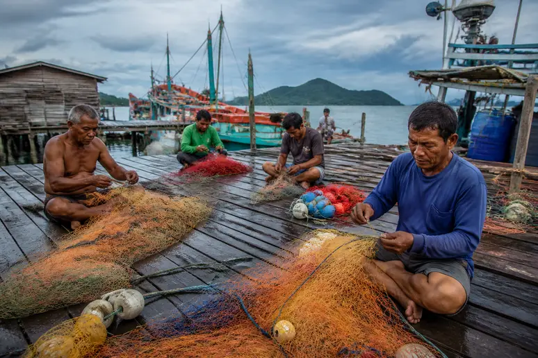 Fischer reparieren Netze in einem thailändischen Dorf, Thailand Wetter Mai, bei teilweis bewölktem Himmel.