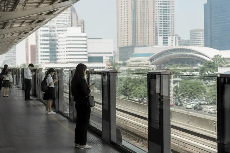 Moderner Bahnsteig des BTS-Netzes in Bangkok mit wartenden Fahrgästen und städtischem Hintergrund