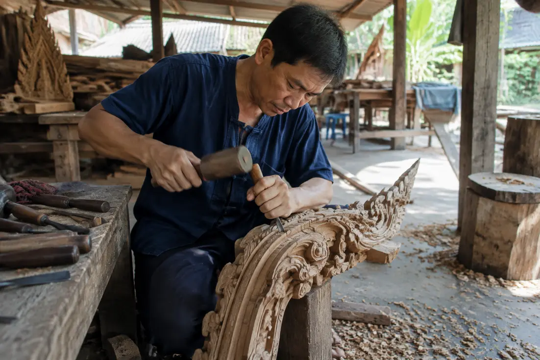 Handwerker schnitzt traditionelles Holzelement in einer offenen Werkstatt in chang rai