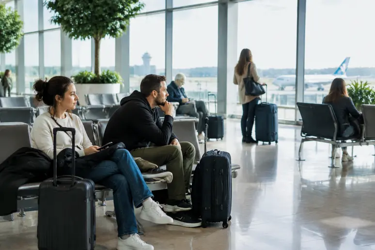 Reisende mit Koffern warten in einer großen Flughafenterminalhalle auf ihren Weiterflug.
