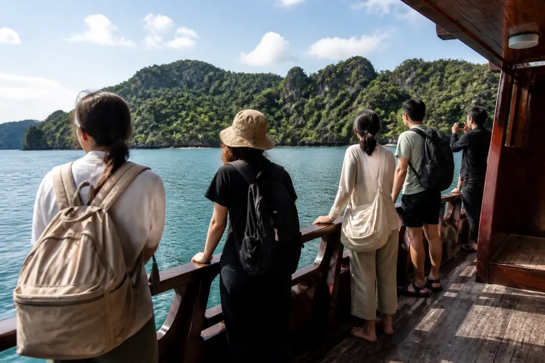 Reisende auf einer Holzfähre mit Blick auf die grüne Tropeninsel im Koh Chang Reiseführer