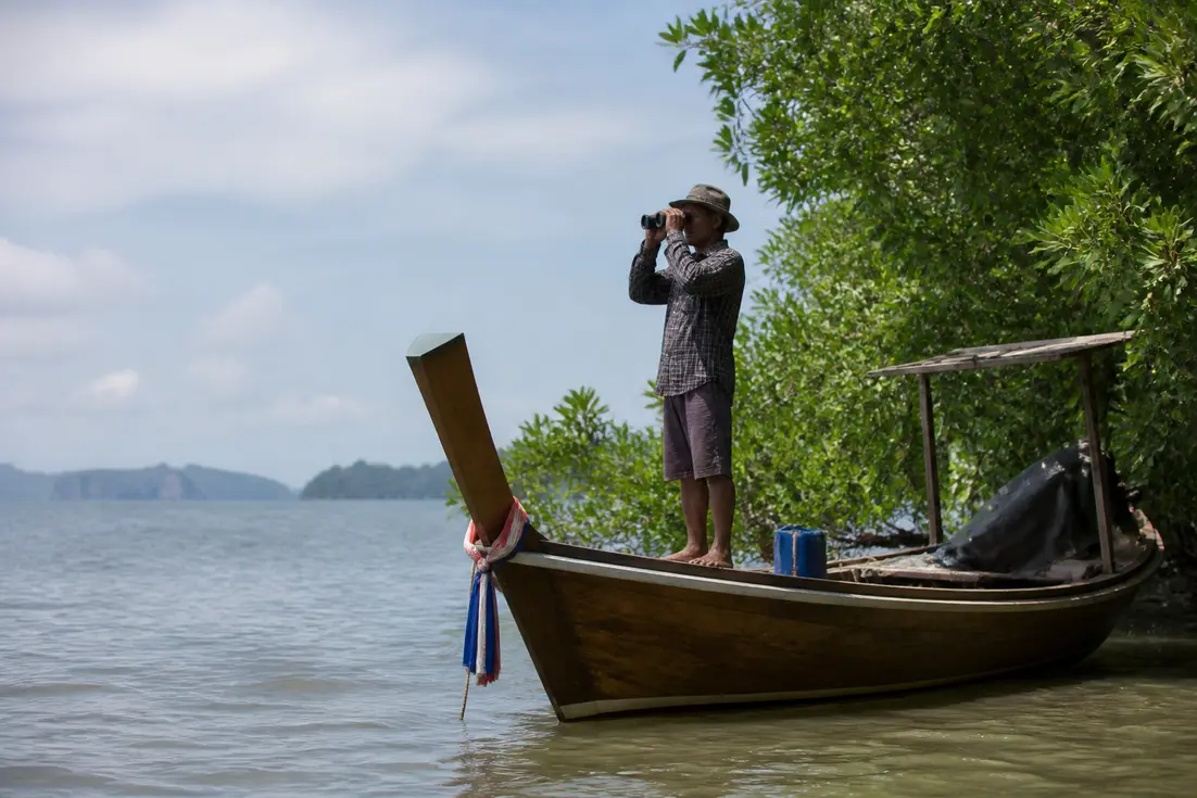 Ein Reiseleiter mit Fernglas auf einem Longtail-Boot im Rahmen eines Koh Libong Reiseführer