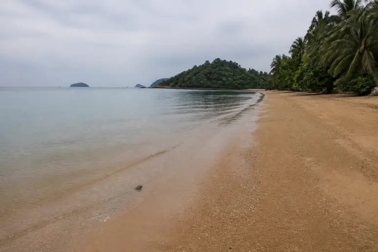 Naturbelassener Strand mit bräunlichem Sand und flachem Wasser an der Westküste von Koh Sukorn