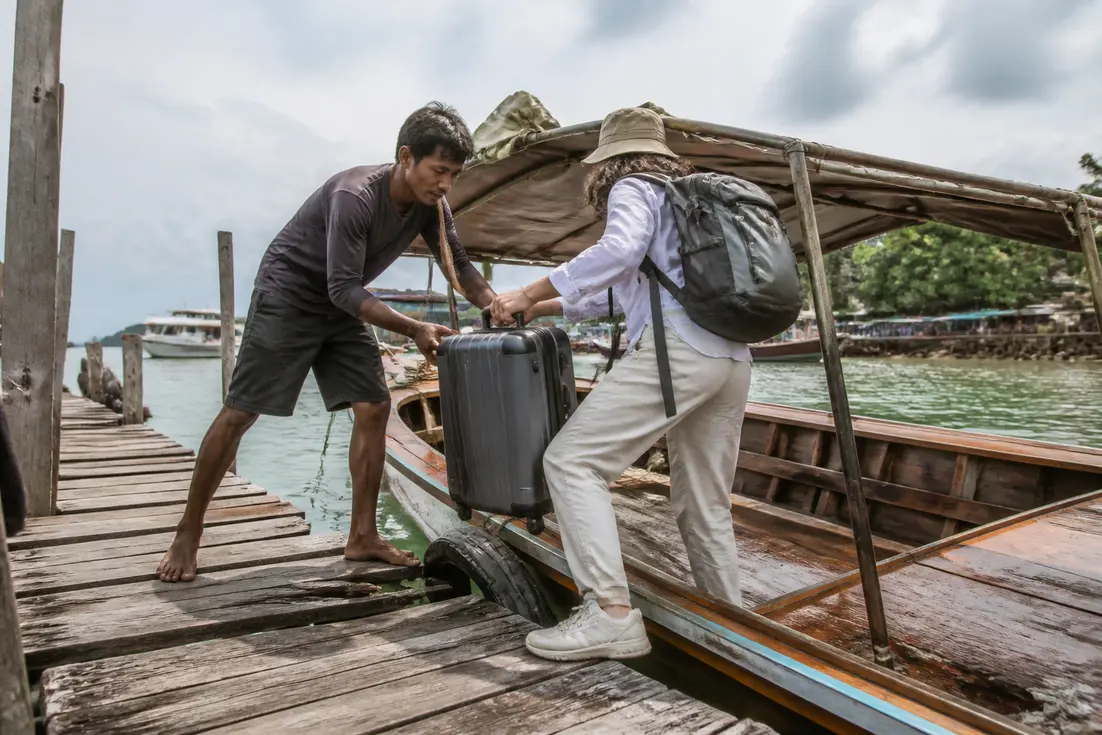 Koh Sukorn Reiseführer: Einheimischer Bootsführer hilft Reisenden beim Einsteigen in ein Holzboot am Pier