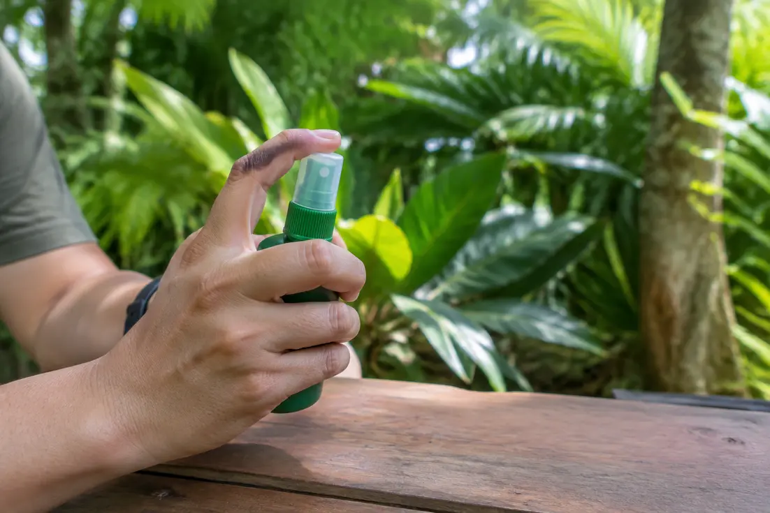 Ein Reisender hält mückenspray thailand bereit auf einem Holztisch im tropischen Garten