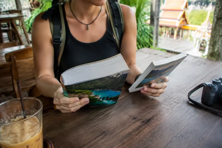 Reisender vergleicht gedruckte Reiseführer auf einem Holztisch in Thailand