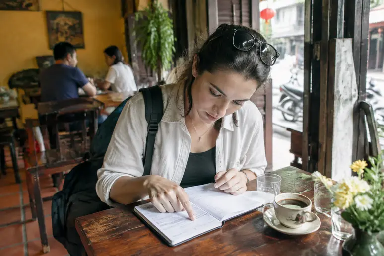 Reisender prüft Reisedaten und Öffnungszeiten für tet 2026 in einem Café