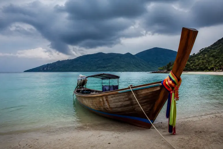 Ein traditionelles Longtail-Boot liegt am Strand eines geschützten Meeresgebiets in Thailand bei bewölktem Himmel