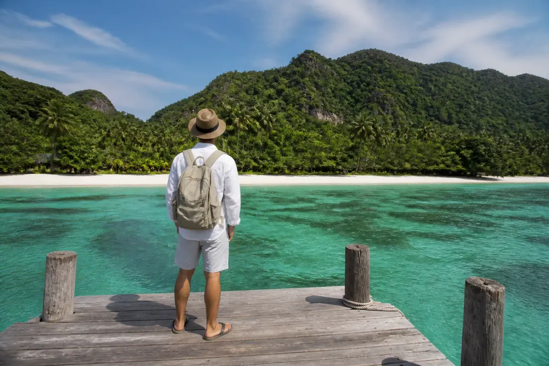 Thailand Urlaub welche Insel: Reisender auf einem Holzsteg vor tropischer Küstenlandschaft