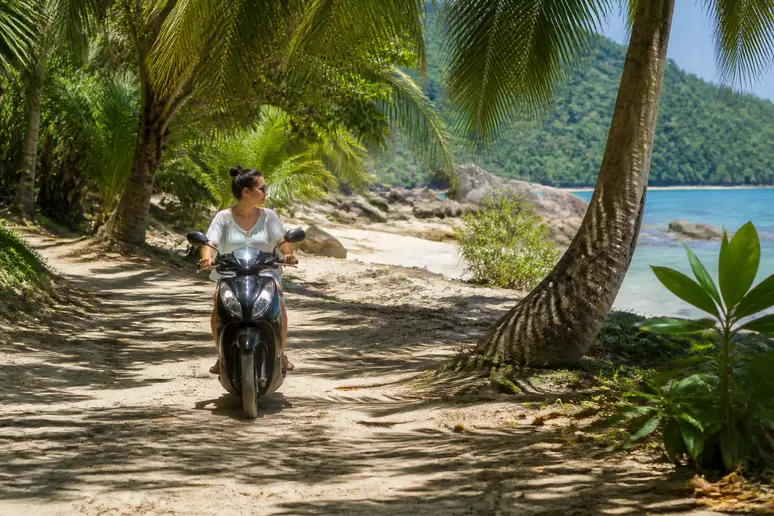 Reisender fährt mit dem Motorroller auf einem sandigen Pfad durch einen Palmenwald für den Urlaub Thailand Inseln.