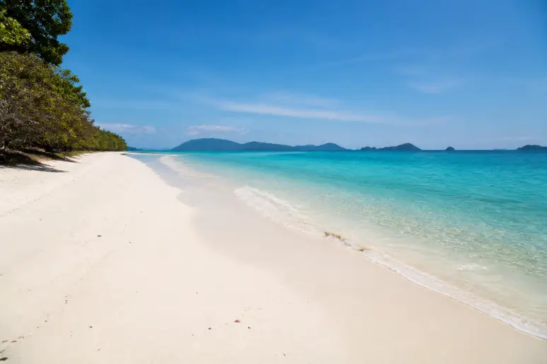 Ruhiger Sandstrand mit klarem blauem Wasser an der thailändischen Westküste während der optimalen Reisezeit.