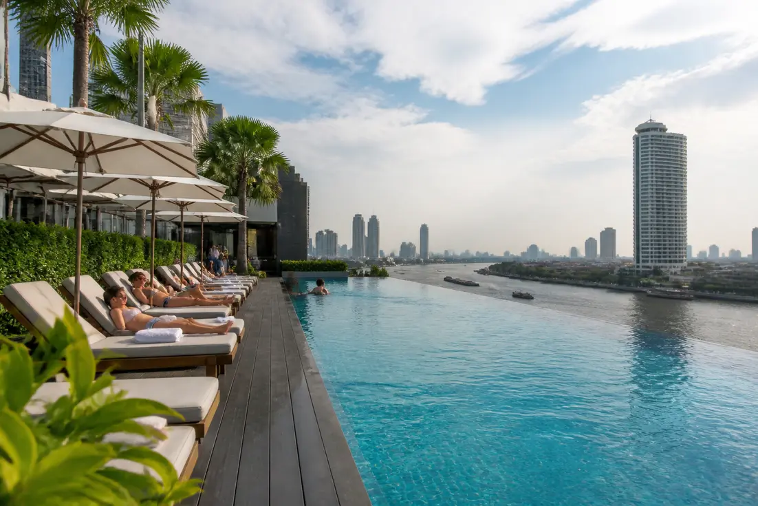 Gäste entspannen am Infinity-Pool im Chatrium Hotel Riverside Bangkok mit Blick auf den Fluss