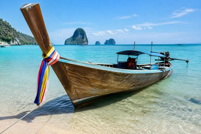Ein traditionelles Longtail-Boot liegt am flachen Sandstrand für die Überfahrt zur Insel Koh Kham bereit.