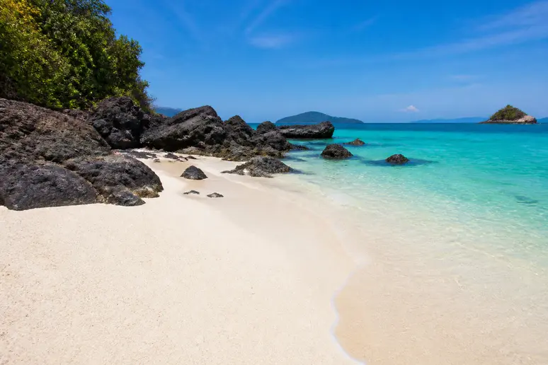 Feiner weißer Sand und dunkle Vulkanfelsen am türkisblauen Strand von Koh Kham Thailand.