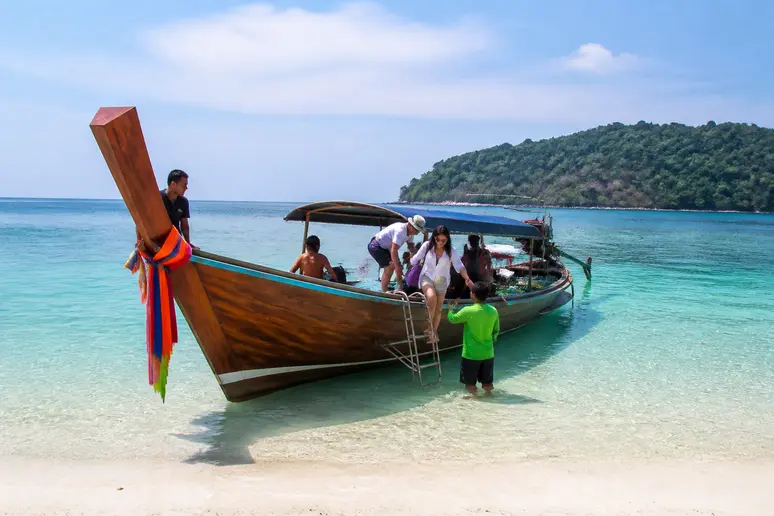 Ein hölzernes Ausflugsboot nähert sich dem flachen Sandstrand für die Überfahrt nach Koh Kham.