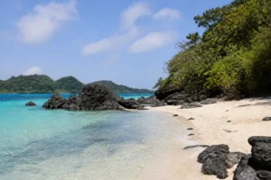 Tropischer Strand mit klarem Wasser und dunklen Felsen auf Koh Kham Thailand
