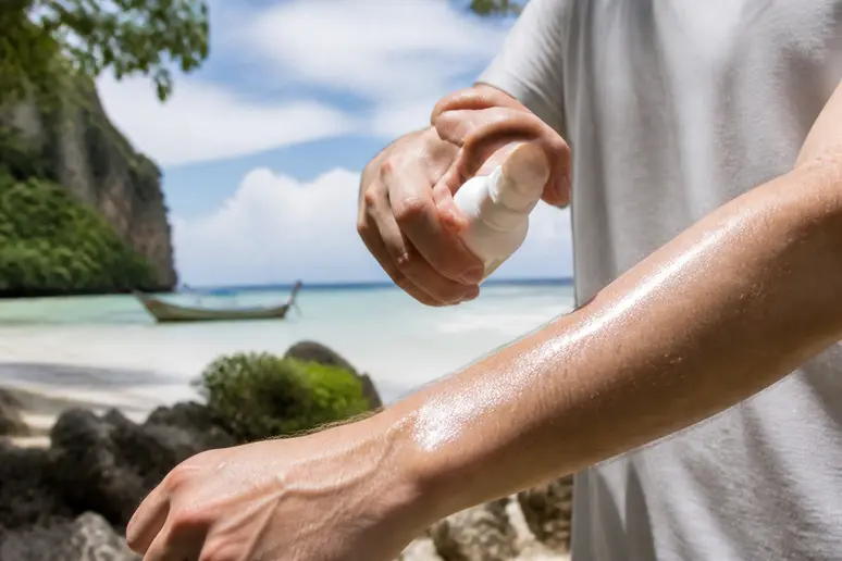 Eine Person trägt am Strand von Koh Kood Mückenschutzmittel auf den Arm auf.