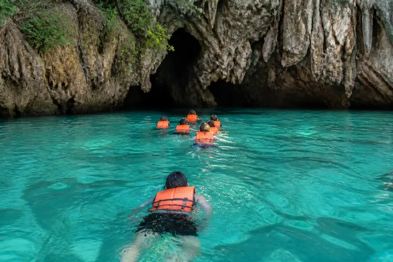 Schwimmer am dunklen Höhleneingang der Emerald Cave auf Koh Mook