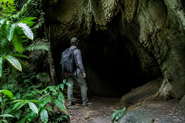 Besucher steht nachdenklich vor dem schmalen Höhleneingang in Chiang Dao