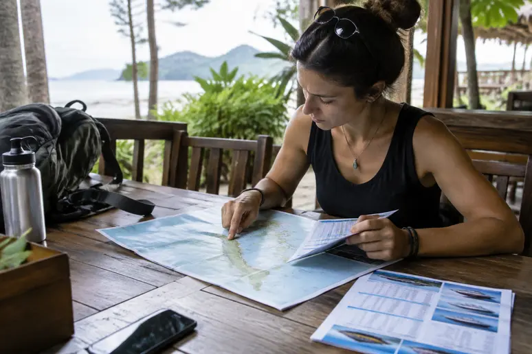 Reiseplaner prüft Fährverbindungen und Landkarte für die thailändische Andamanensee auf einem Holztisch